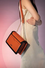 Women's leather shoulder bag in orange colour and black binding with gold twist lock and retractable gold chain strap by JULKE