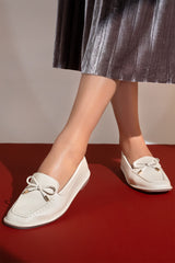 Women's flat moccasin style shoes in off white colour and leather texture with matching bow and flexible transparent rubber sole by JULKE. 