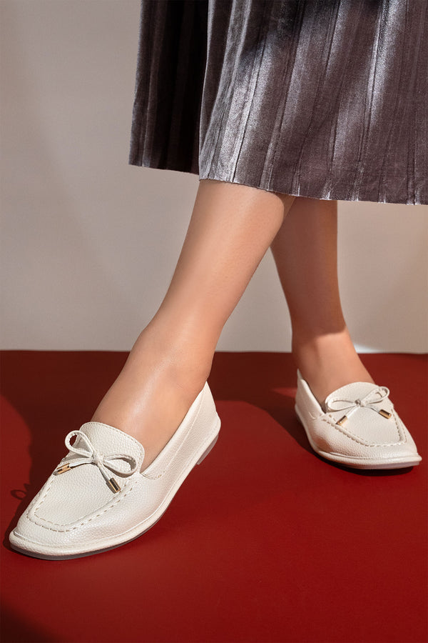 Women's flat moccasin style shoes in off white colour and leather texture with matching bow and flexible transparent rubber sole by JULKE. 